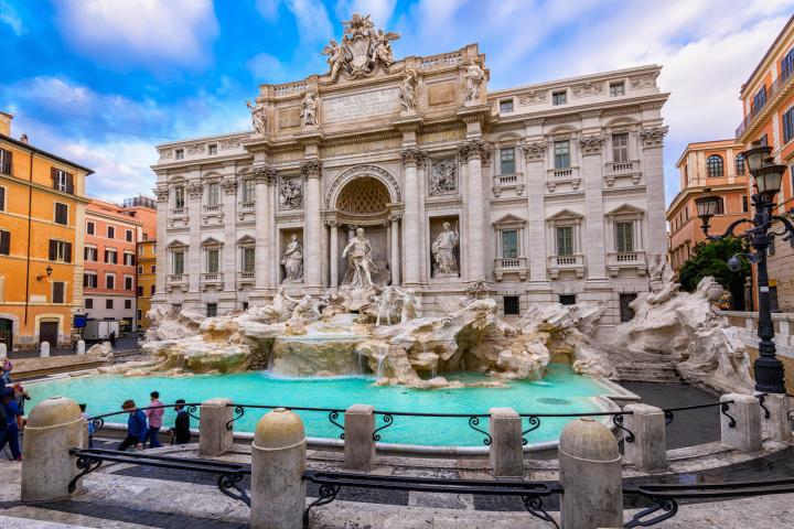 a person sitting on a bench in front of a stone building with Trevi Fountain in the background